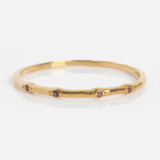 The Solid Gold Textured Birthstone Stacking Ring features a thin, organic-shaped gold band with small, evenly spaced purple gemstones, shown on a plain white background.