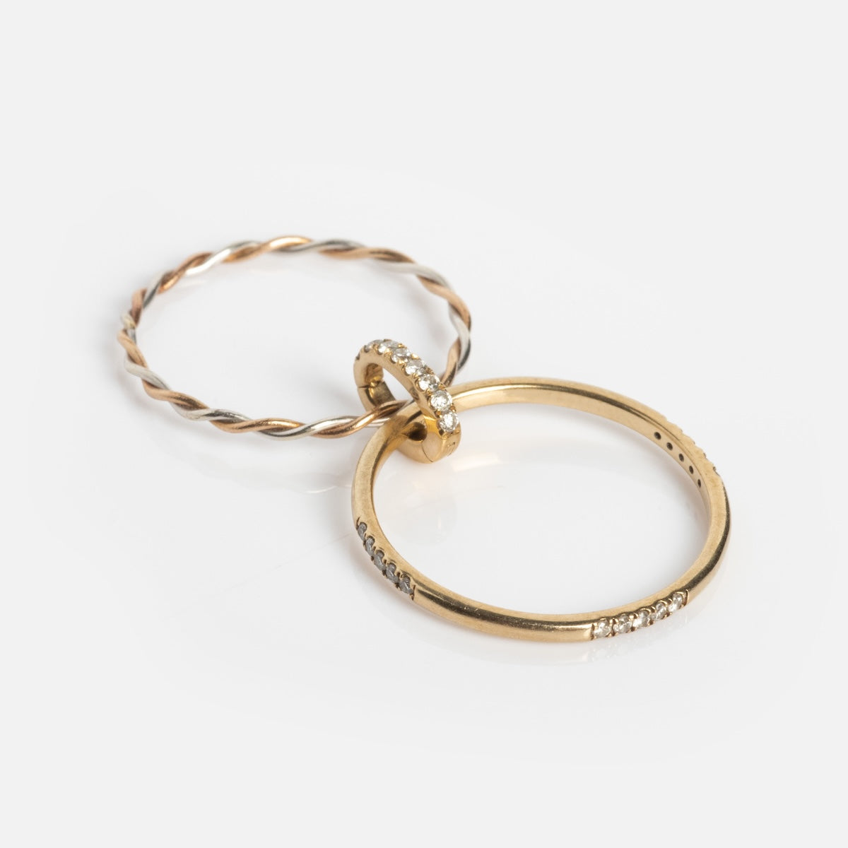 The Solid Gold Dainty Diamond Stacking Ring, set with lab created diamonds along a smooth gold band, is shown next to a thin twisted solid gold ring on a white background.