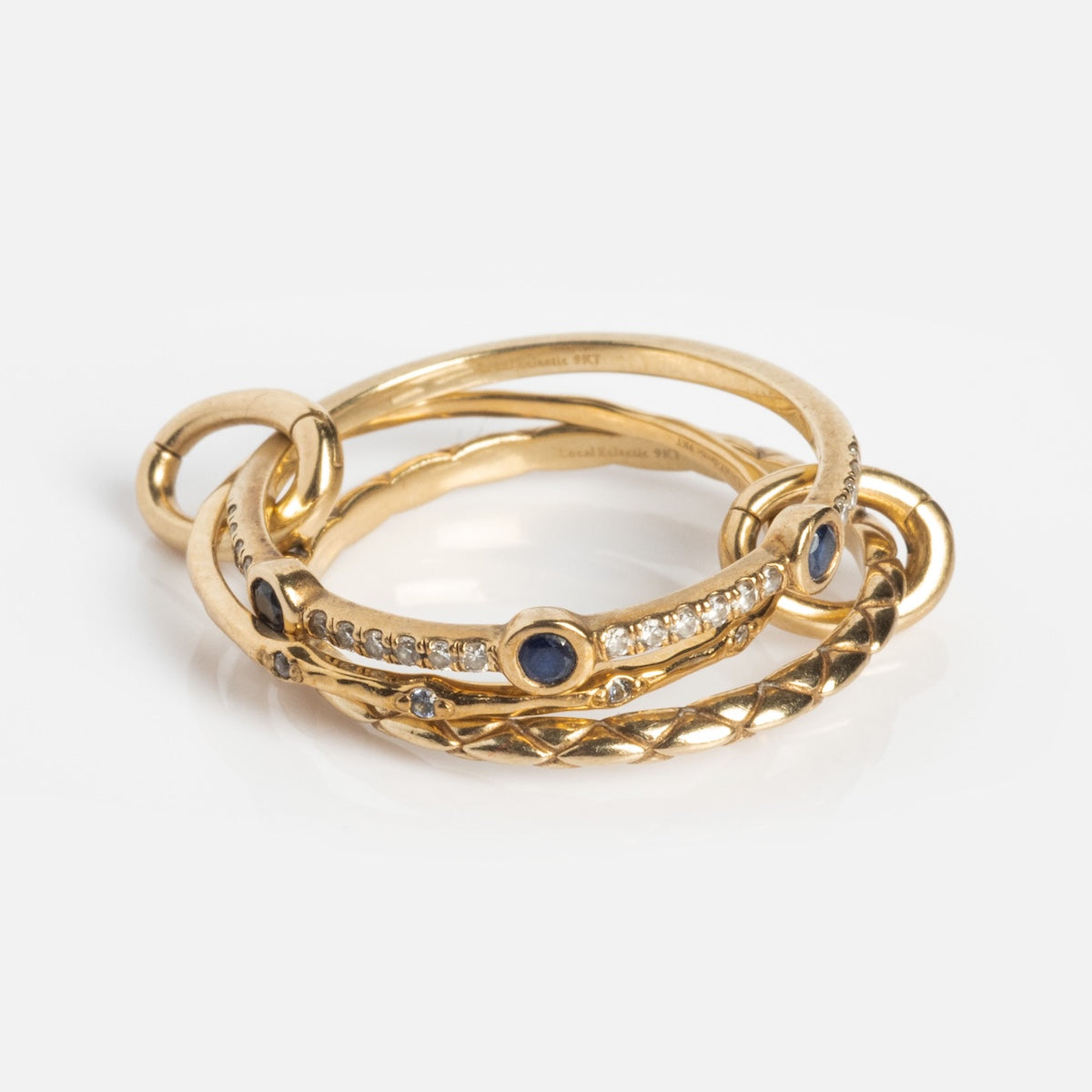 The Solid Gold Ring Clip features blue gemstones, diamond accents, and engraved patterns—three gold rings linked together for a perfect DIY stack, displayed against a plain white background.