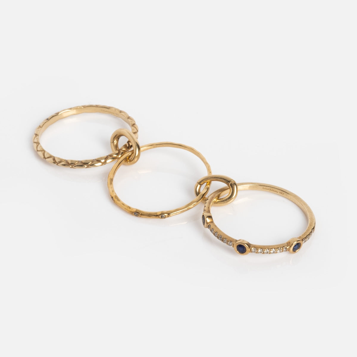 The Solid Gold Ring Clip features four linked rings—textured, plain, hammered, and gemstone-accented—for a customizable and stunning stack, displayed on a white background.