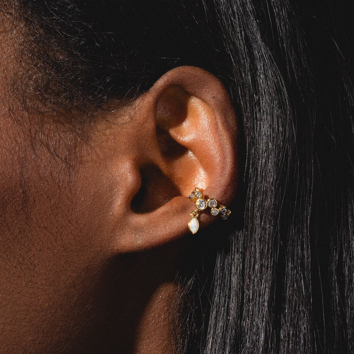 Close-up of a person with straight black hair wearing the Sparkle Drop Ear Cuff—gold, sparkling, and adorned with small round and teardrop gemstones. Perfect as no-piercing earrings.