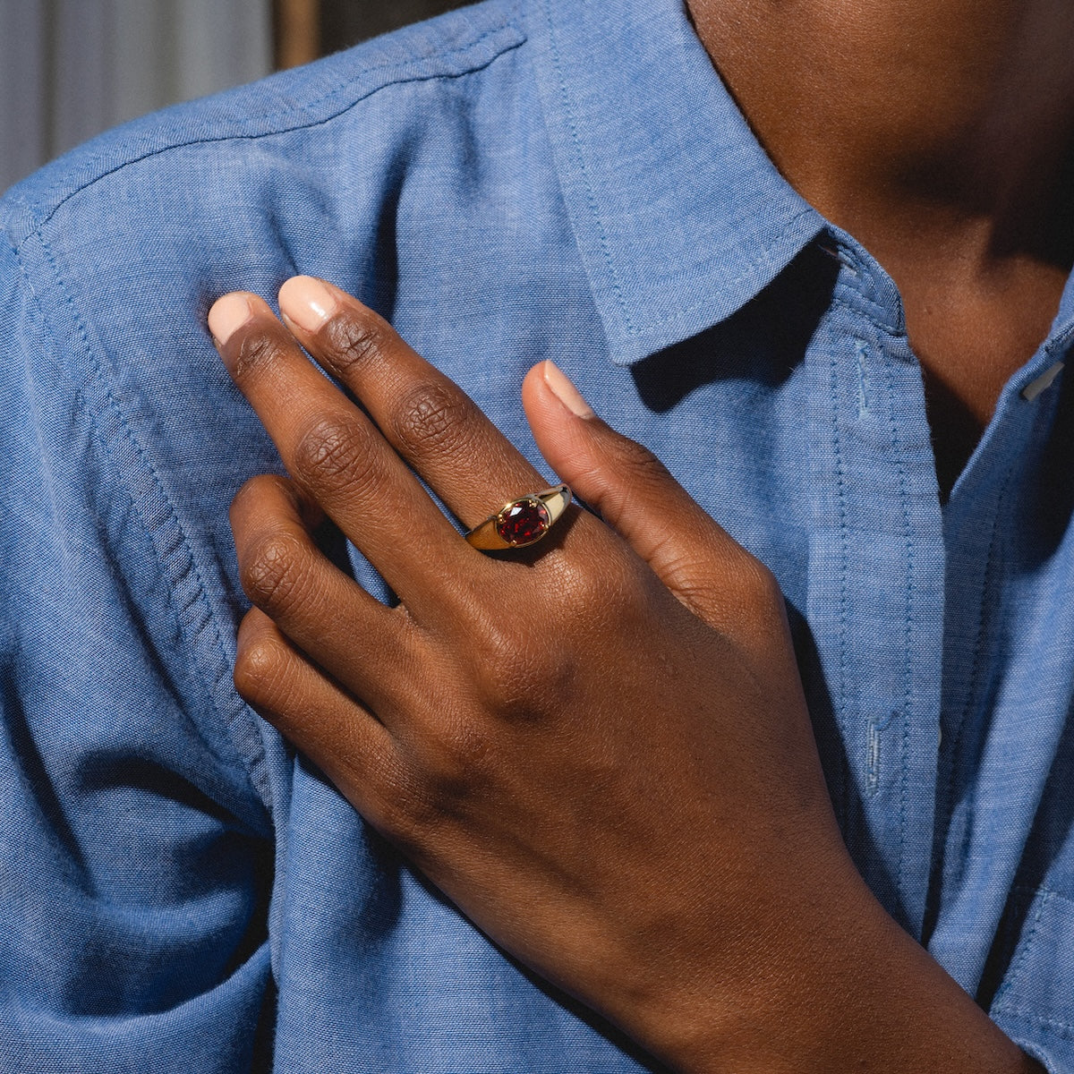 Hand wearing a ring with a red gemstone against a blue shirt