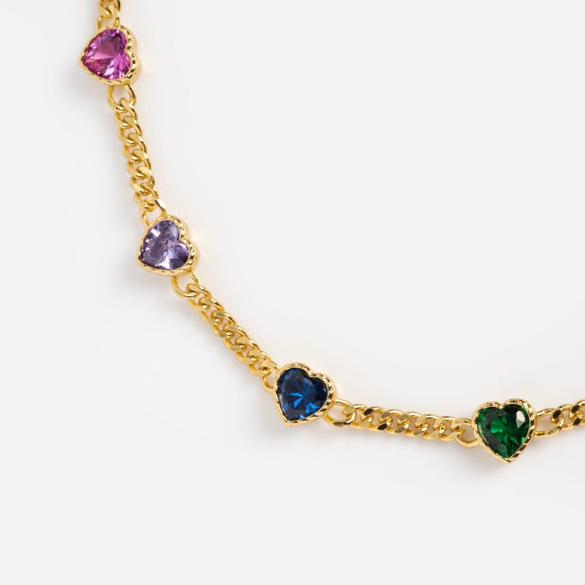 The Love Prism Rainbow Heart Necklace is a 14k gold plated piece featuring heart-shaped gems in purple, pink, blue, green, and light purple, evenly spaced along the chain and set against a white background.