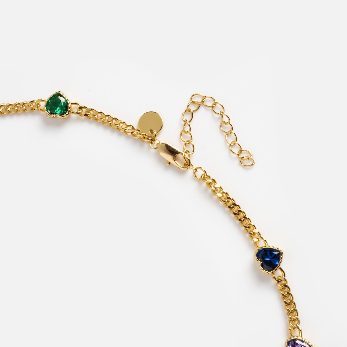Close-up of the Love Prism Rainbow Heart Necklace, a 14k gold plated chain with multicolor heart gems—including green and dark blue—on a white background. Features a lobster clasp and adjustable extender.