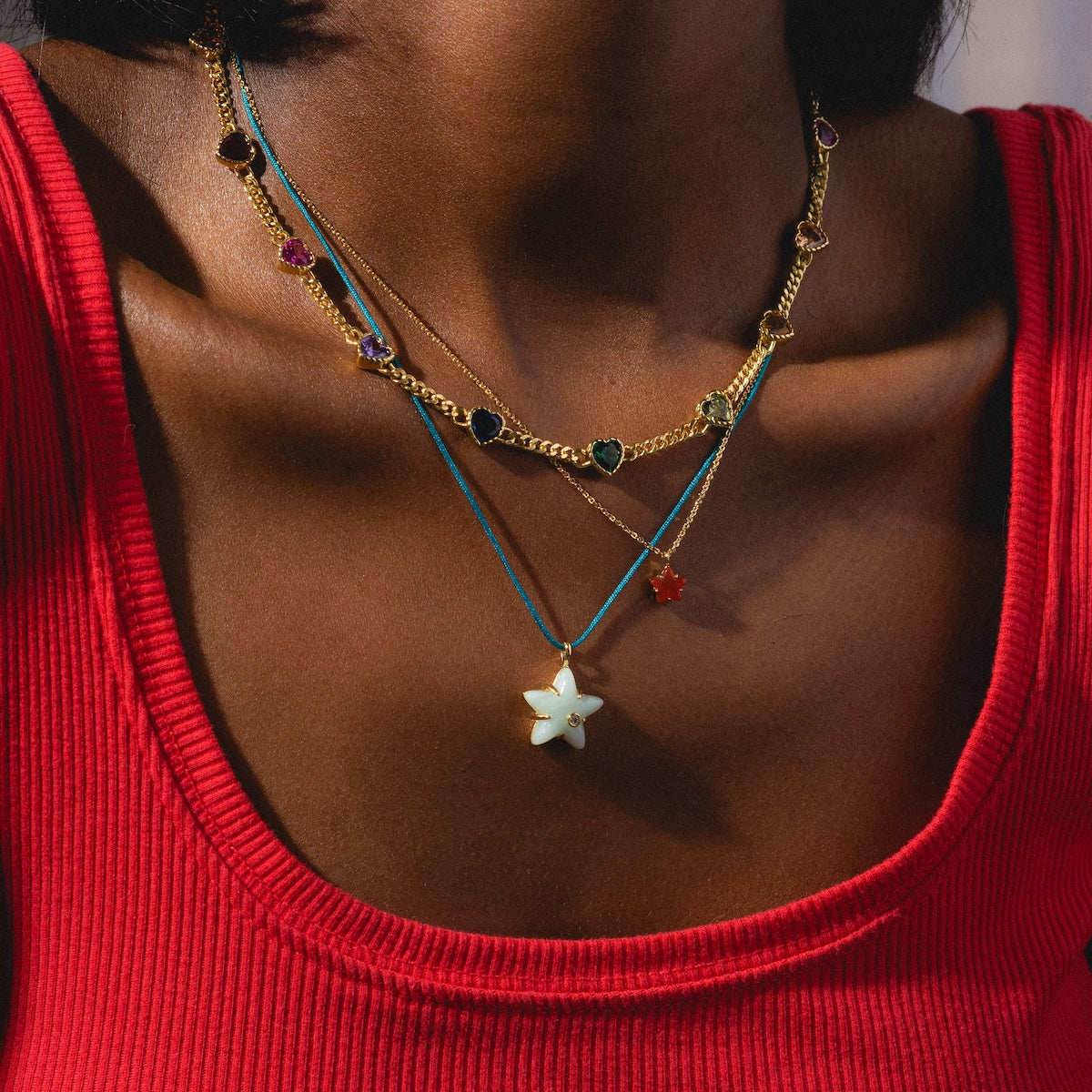 Close-up of a person wearing a red top with layered necklaces featuring star-shaped pendants.