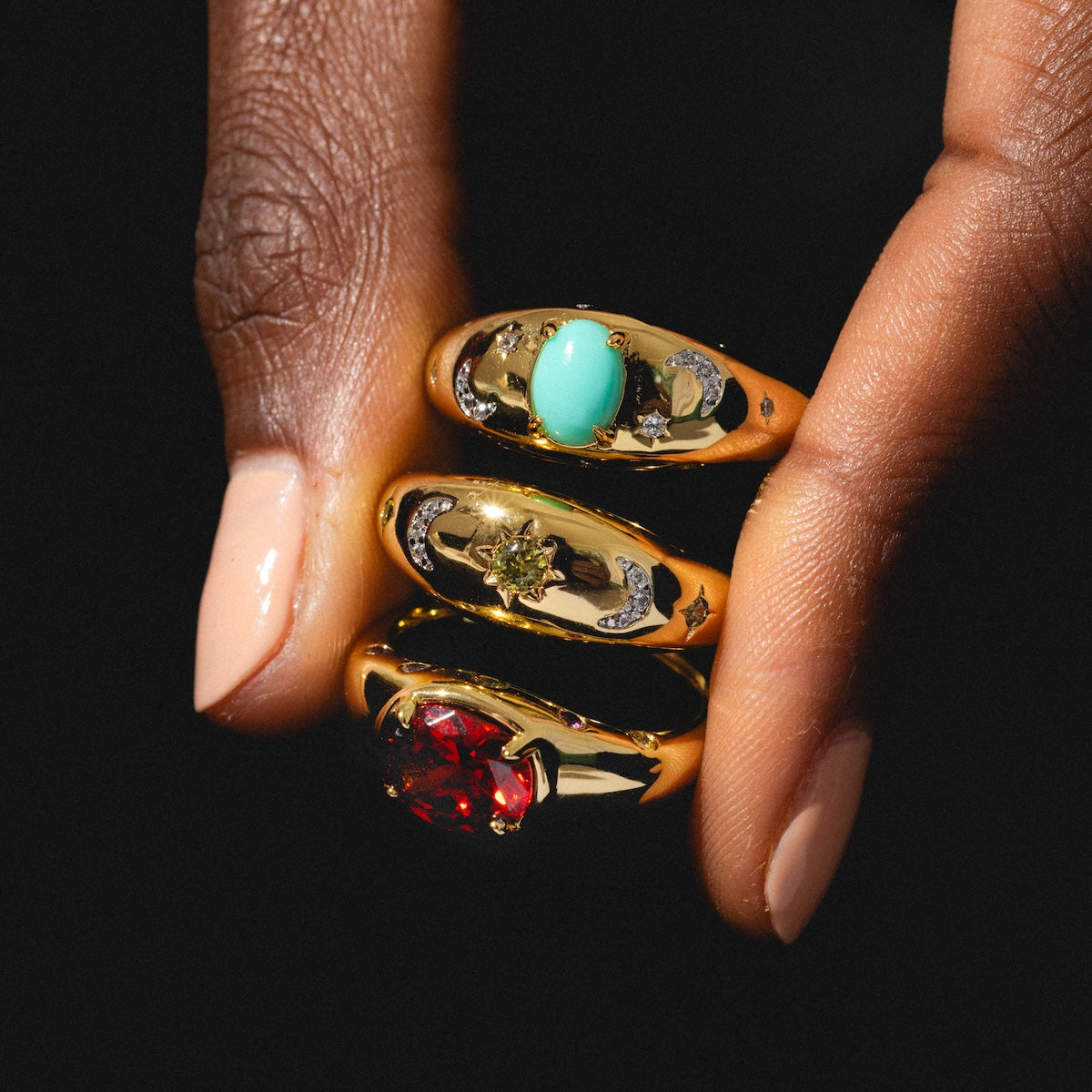 Gold rings with gemstones on a hand against a black background