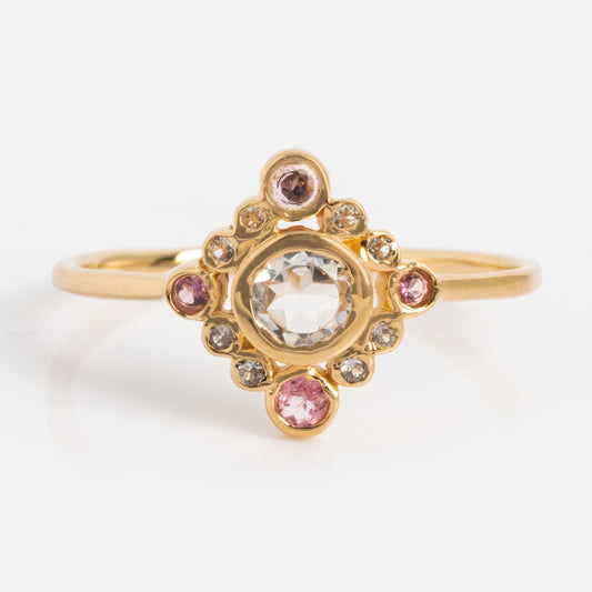 The Oberoi Ring is a yellow gold plated tourmaline ring with a central round clear stone, accented by smaller pink and clear gems in an ornate, symmetrical multi-stone design.