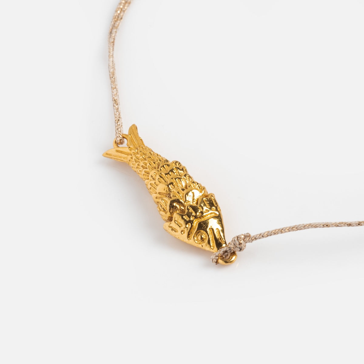 The Sardina Bracelet features a detailed gold fish charm inspired by Sophie Deschamps Bijoux, attached to a simple beige cord and shown against a plain white background.