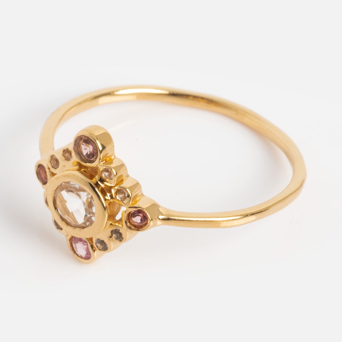 The Oberoi Ring is a delicate yellow gold plated piece featuring a central clear gemstone, accented by smaller pink and clear stones in a decorative multi-stone design, shown against a plain white background.