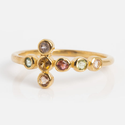 The Notre Dame Ring is a yellow gold plated ring with seven small, multicolor tourmaline gemstones in a sideways cross design, shown on a white background.