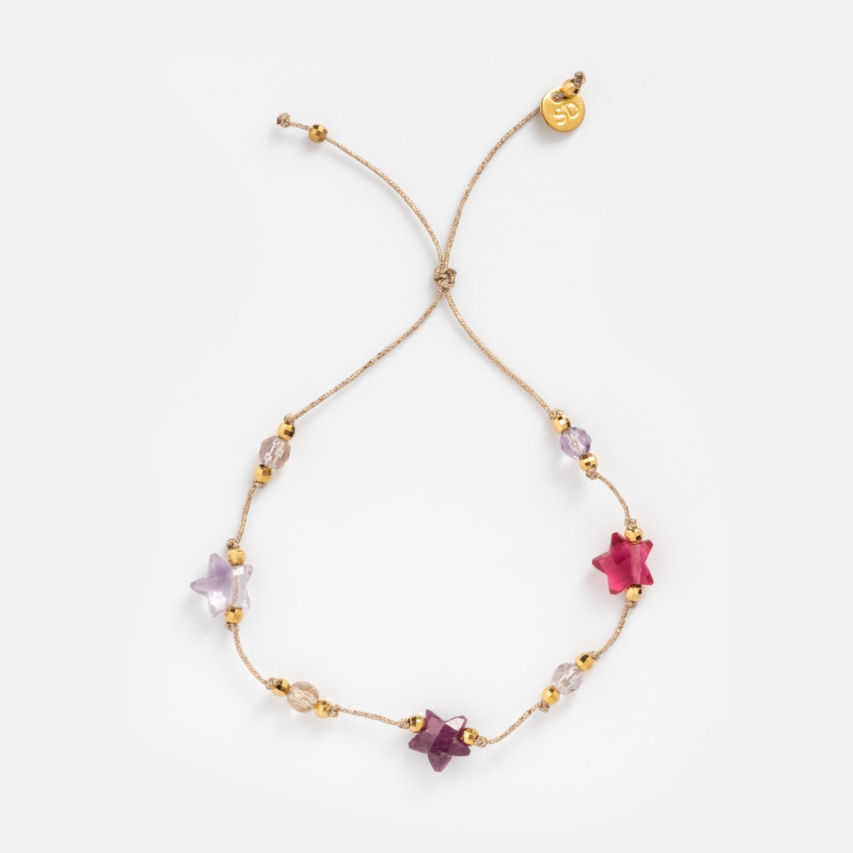 The Martha Bracelet features delicate gold-plated beads, five star-shaped beads in pink, purple, and clear tones, plus a gold charm with an engraved design at the end. Its adjustable for the perfect fit and adds a touch of elegance to any look.