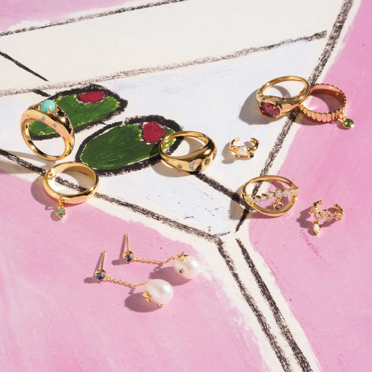 Collection of gold jewelry including rings and earrings on a pink and white surface.