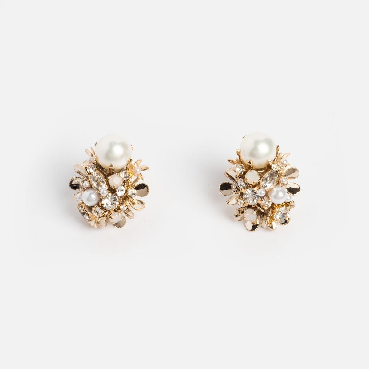 The Luxe Pearl and Crystal Cluster Earrings feature gold plating, clusters of shiny crystals, metallic accents, and a prominent round pearl at the top, all displayed against a plain white background.
