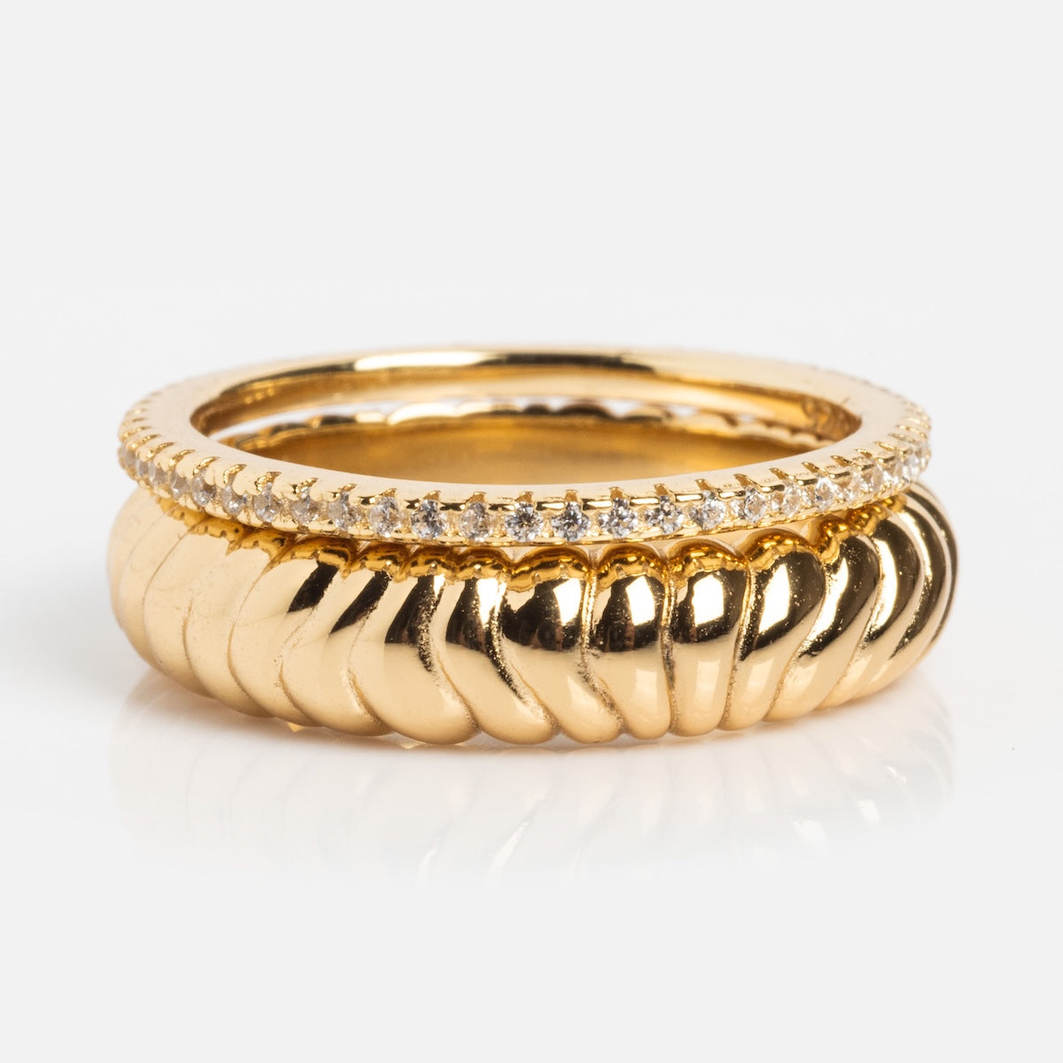 The Reagan Ring Set includes a bold 14k yellow gold plated twisted ring and a slim band with sparkling white gemstones, both beautifully displayed against a crisp white background.