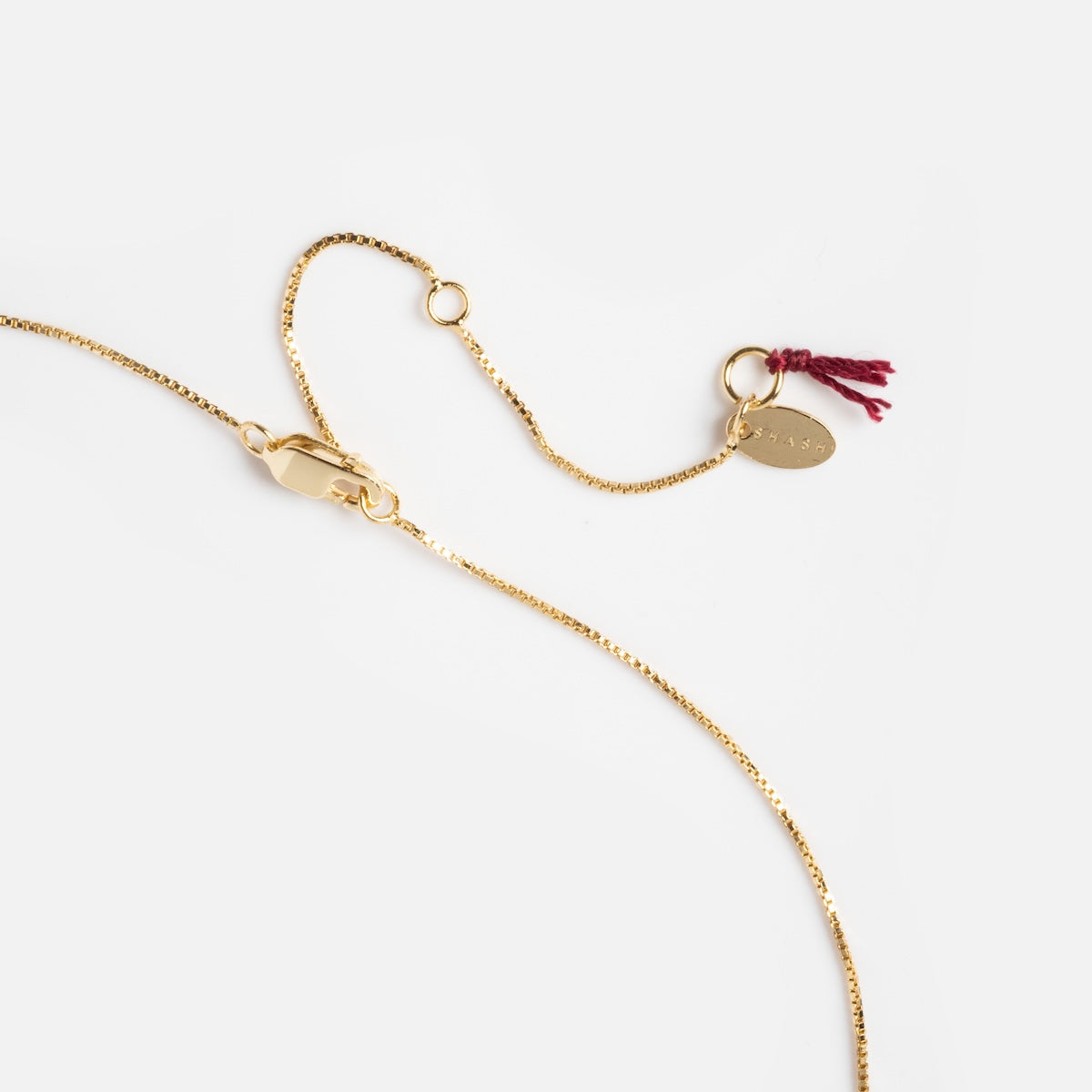 The Baguette and Pear Cushion Pendant Necklace features a delicate 14k gold vermeil chain, lobster clasp, small oval tag, and tiny red thread detail, shown against a white background.