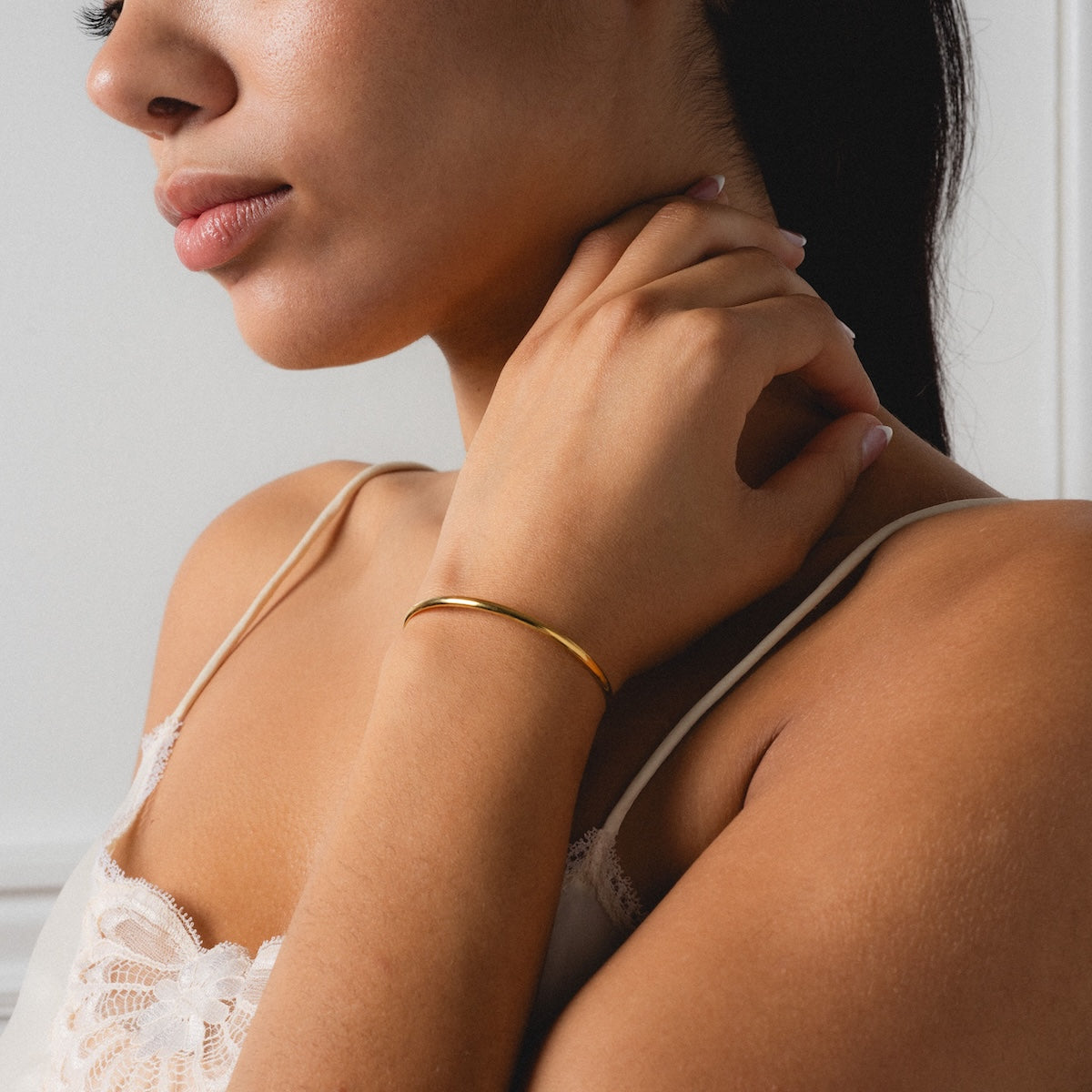 A woman in a white lace camisole touches her neck, highlighting the delicate Bar Chain Bracelet Cuff on her wrist. The close-up image focuses on her jewelry and soft expression from the shoulders up.