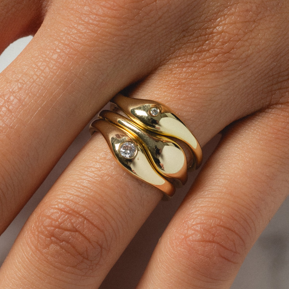 A close-up of a hand wearing the Delphine Solitaire Ring Set—yellow gold rings with wavy designs and small diamonds—styled on adjacent fingers for a modern, elegant look.