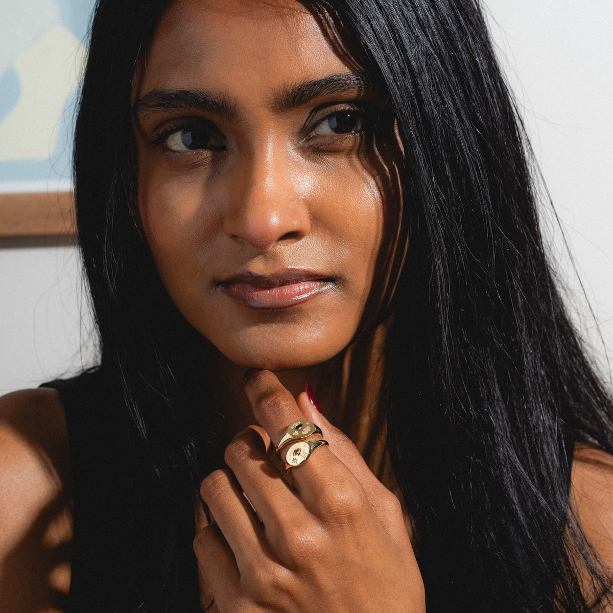 Woman with long black hair and gold manifestation rings on her finger, wearing a black top.
