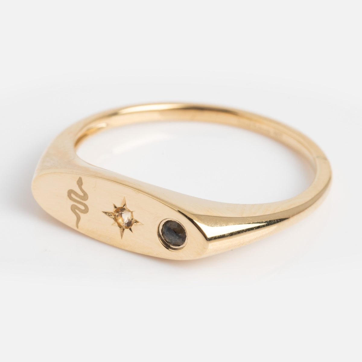 Side of gold manifestation ring with engraved designs on a light background