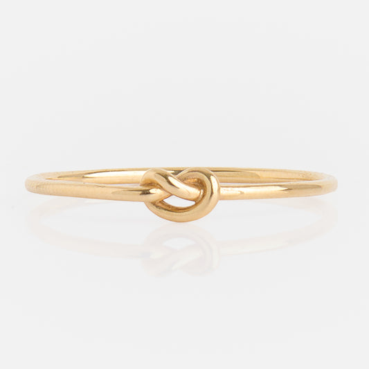 The Solid Gold Simple Knot Ring is a slender 10k yellow gold ring with a delicate knot centerpiece, showcased on a plain white background.