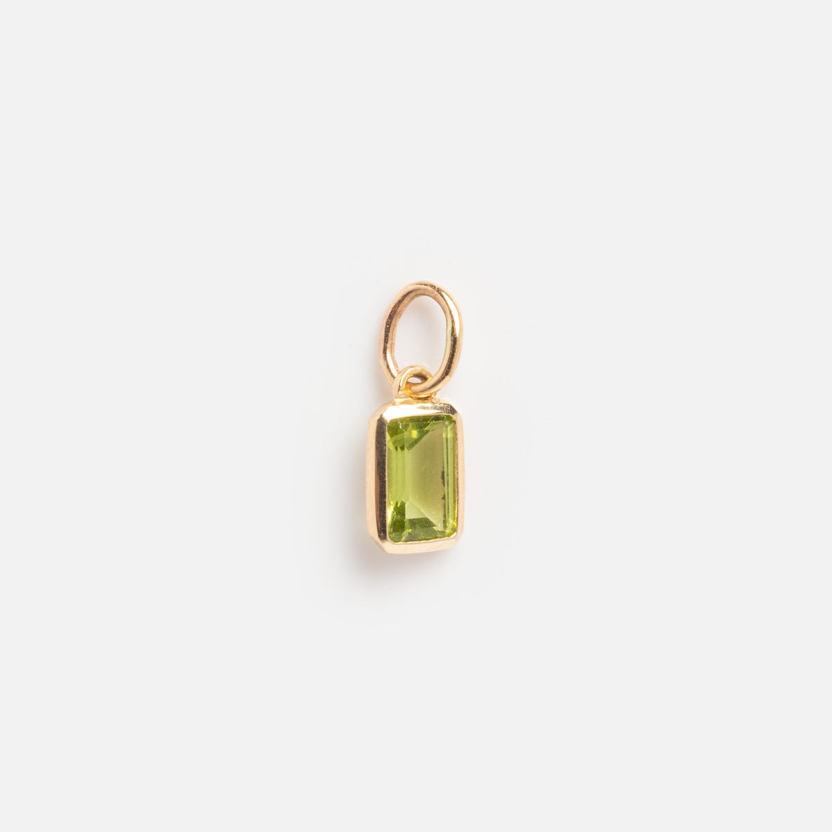 The Solid Gold Birthstone Baguette Charm August Sample is a small gold pendant with a rectangular, faceted green gemstone and an attached gold loop, displayed on a plain white background.
