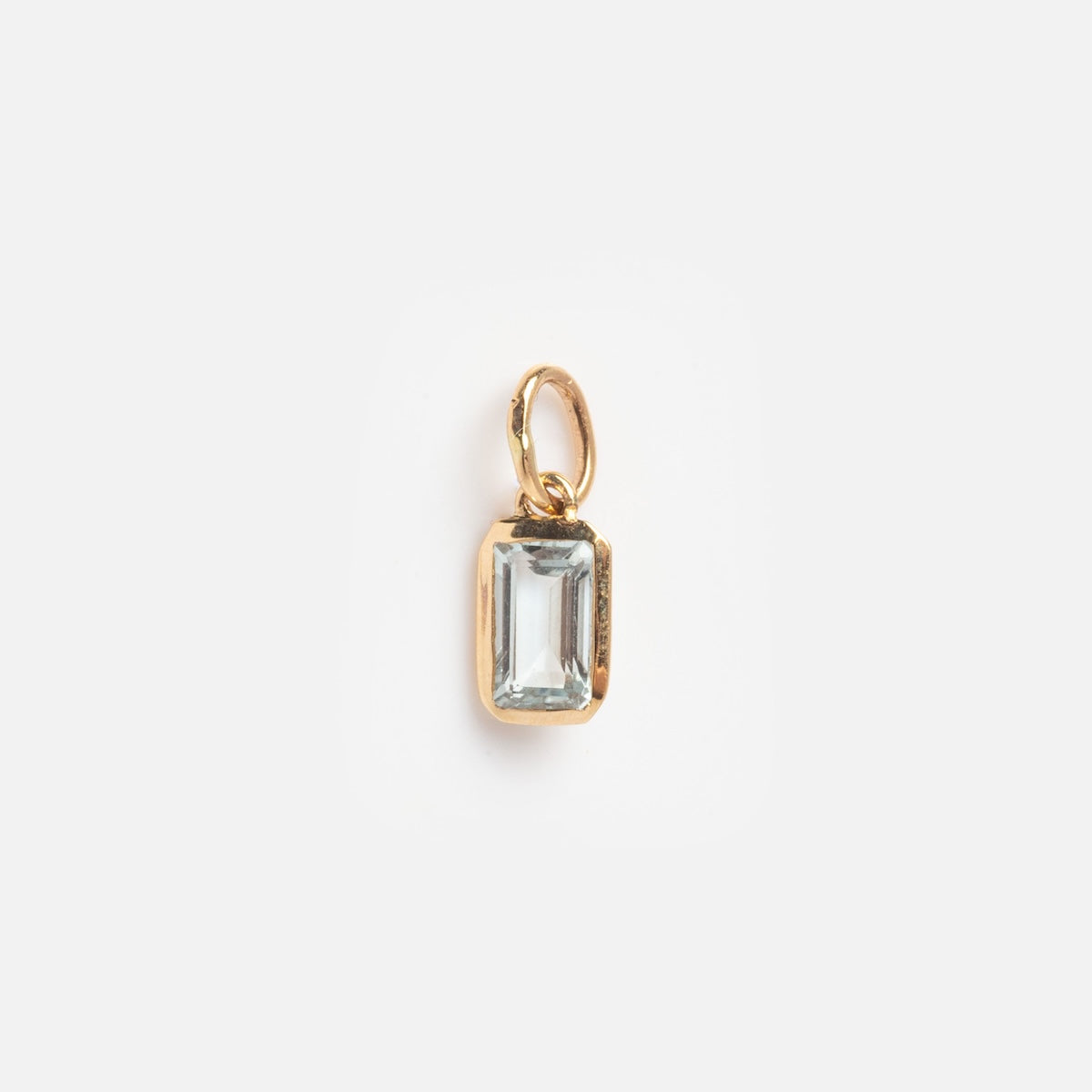 The Solid Gold Birthstone Baguette Charm March Sample is a small gold pendant with a rectangular clear gemstone in a simple gold frame and loop, shown on a plain white background.