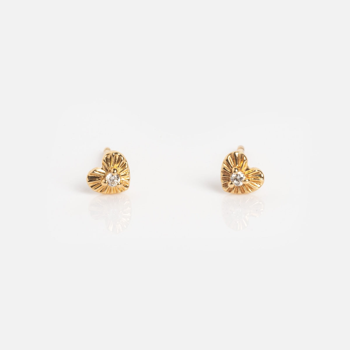 The Solid Gold Heart Stud Earrings Sample features small heart-shaped studs with a textured gold finish and a central clear gemstone, beautifully displayed on a white background.