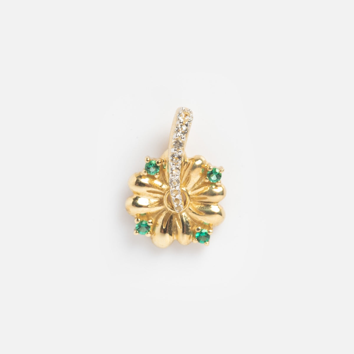 The Solid Gold Lucky Charm is a flower-shaped gold pendant featuring four green gemstones at the edges and a curved row of small white stones in the center, shown on a plain white background.