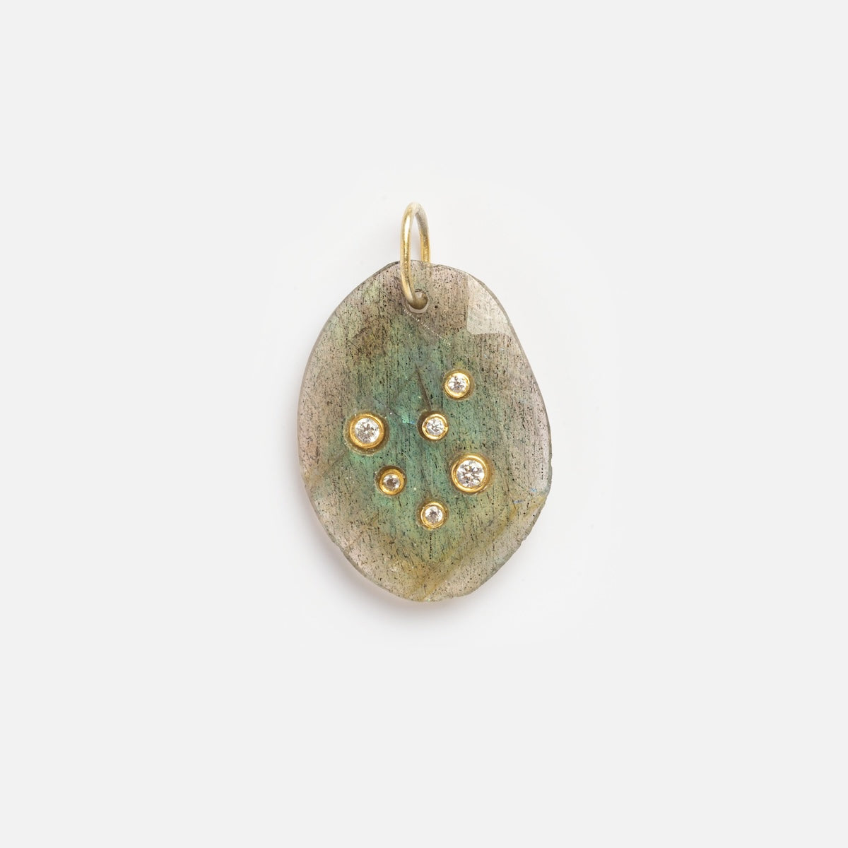 The Labradorite Libra Constellation Charm Sample is an oval pendant with a greenish, textured surface, adorned with seven round gold and diamond-like studs in a scattered pattern, and finished with a small gold loop at the top.
