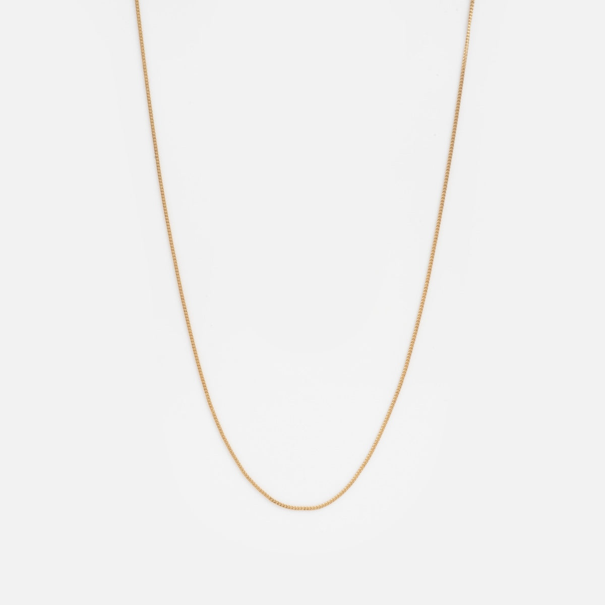 The Solid Gold Delicate Curb Chain Sample, a simple and thin gold necklace, is elegantly displayed against a plain white background.