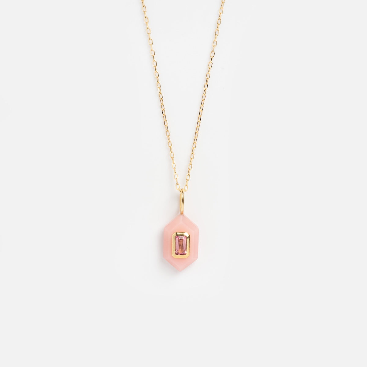 The Solid Gold Large Aura Necklace Pink Sample features a gold chain and a pink hexagon pendant with a rectangular gemstone at its center, shown on a plain white background.