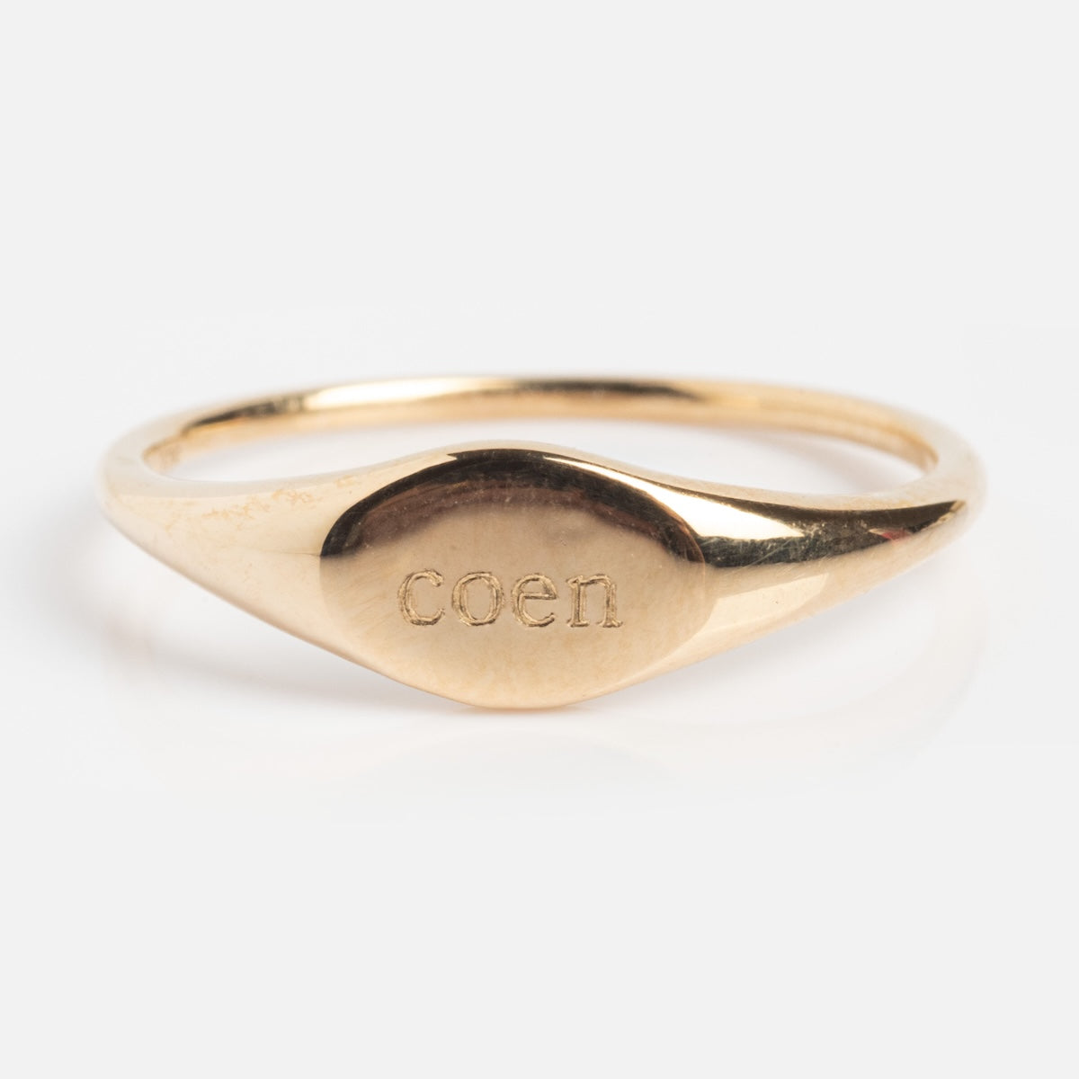 A simple 9k solid yellow gold signet ring, sample size 7, engraved with COEN on its oval face. The Solid Gold Engravable Simple Signet Ring is shown against a white background.