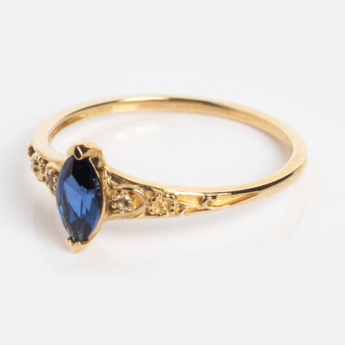 The Solid Gold 2025 September Capsule Classic Blue Sapphire Statement Ring features ornate detailing and a marquise-cut lab-created blue sapphire set at the center, shown against a white background.