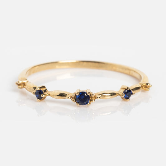 The Solid Gold 2025 September Capsule Delicate Blue Sapphire Stacking Ring features three evenly spaced lab-created blue sapphires in simple prong settings on a 9k yellow gold band, shown against a white background.