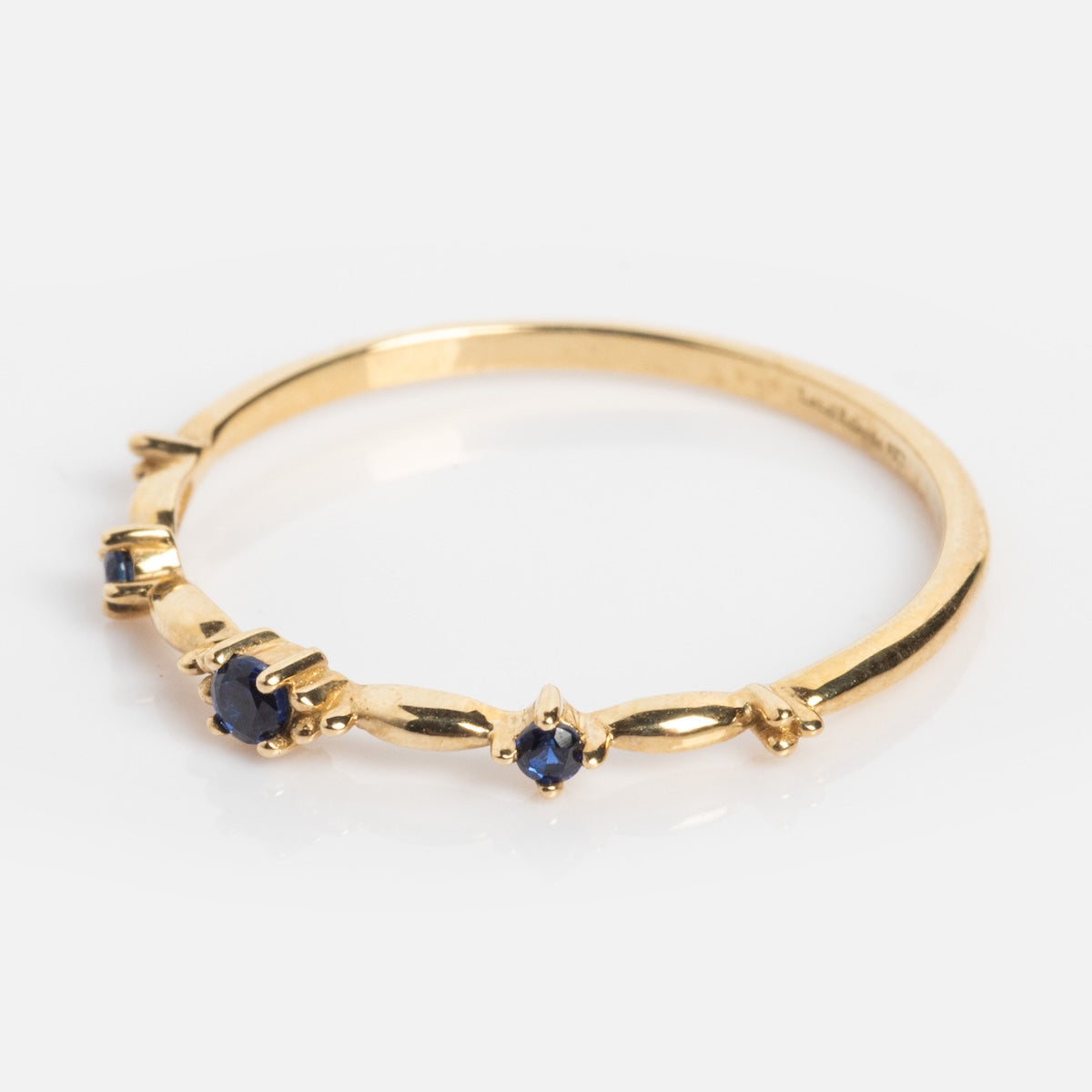 The Solid Gold 2025 September Capsule Delicate Blue Sapphire Stacking Ring features small lab-created blue sapphires set along a minimalist 9k yellow gold band, showcased on a white background.