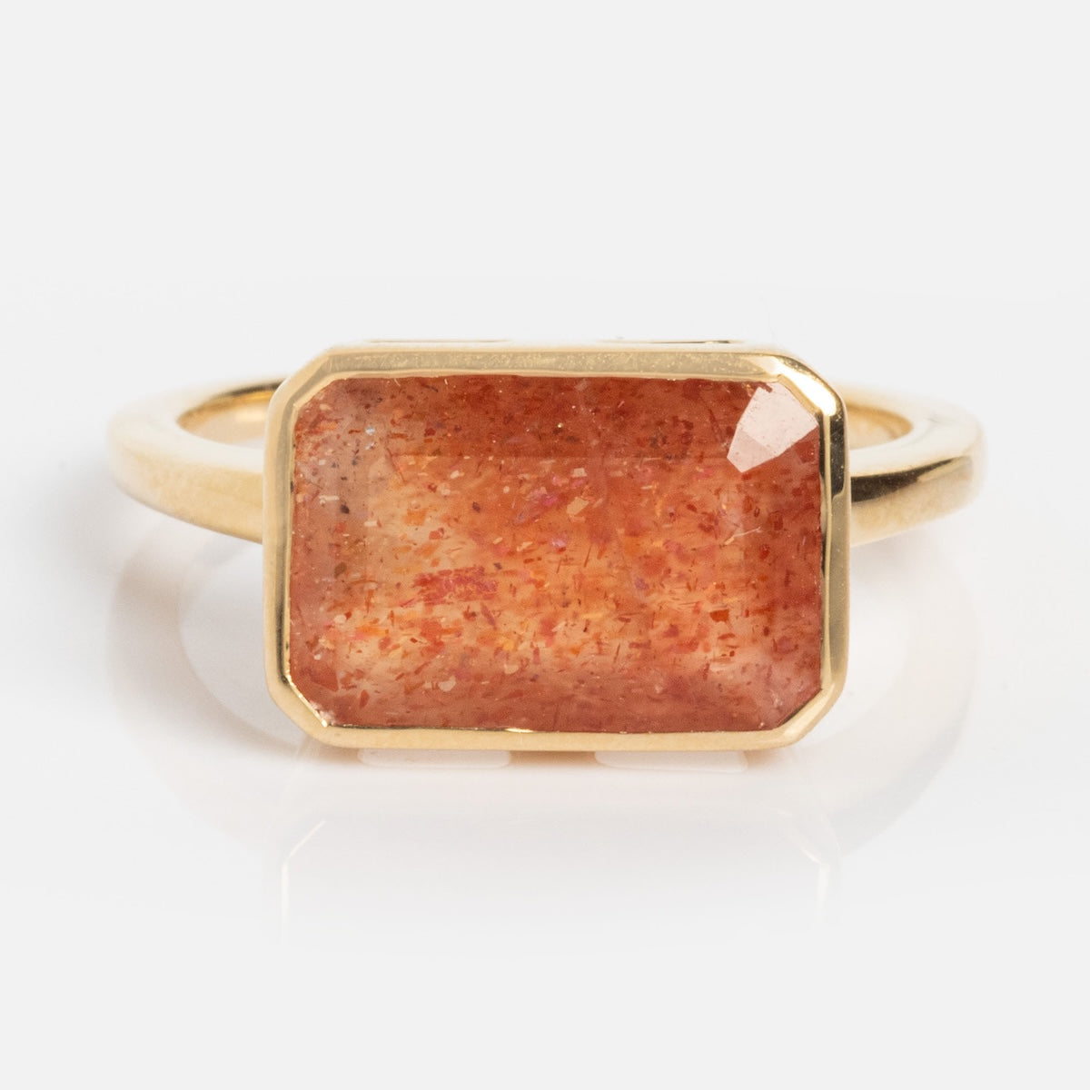 The 14k Jojo Ring features a large, rectangular sunstone with vibrant orange and red hues, set in solid yellow gold with a minimalist bezel setting.