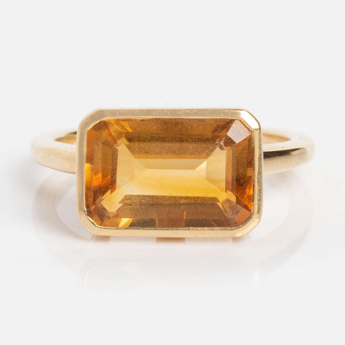 A modern heirloom, the 14k Jojo Ring showcases a large, rectangular, faceted amber gemstone set in solid yellow gold with a simple, elegant band, presented against a plain white background.