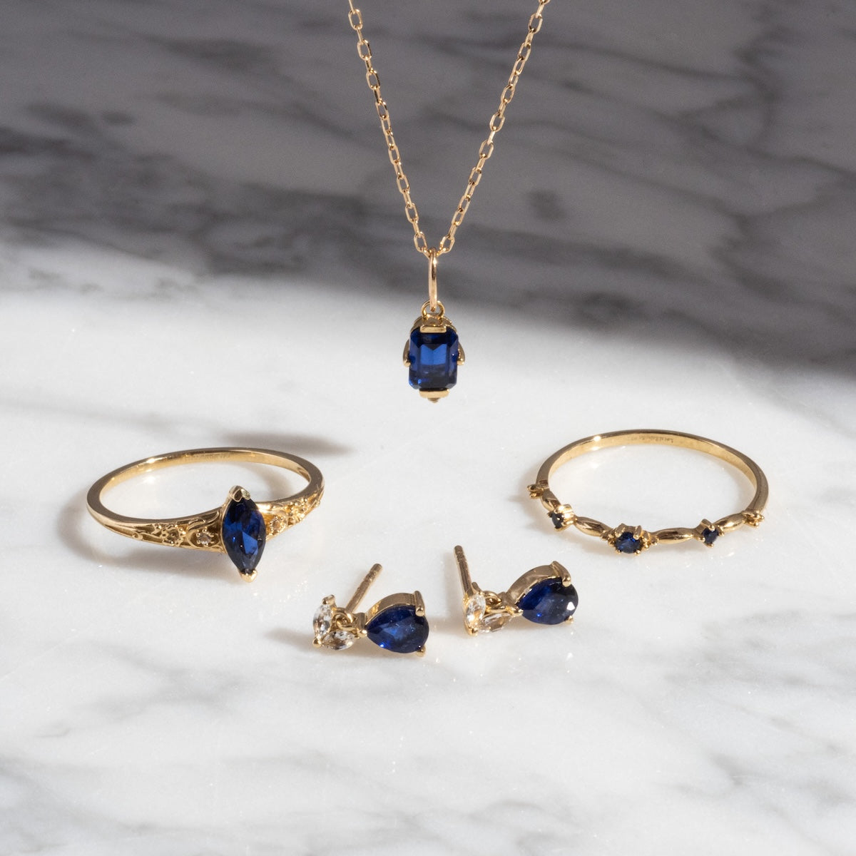 The Solid Gold 2025 September Capsule Classic Blue Sapphire Statement Ring features a lab-created blue sapphire set in 9k solid yellow gold, shown elegantly on a white marble surface under soft light.