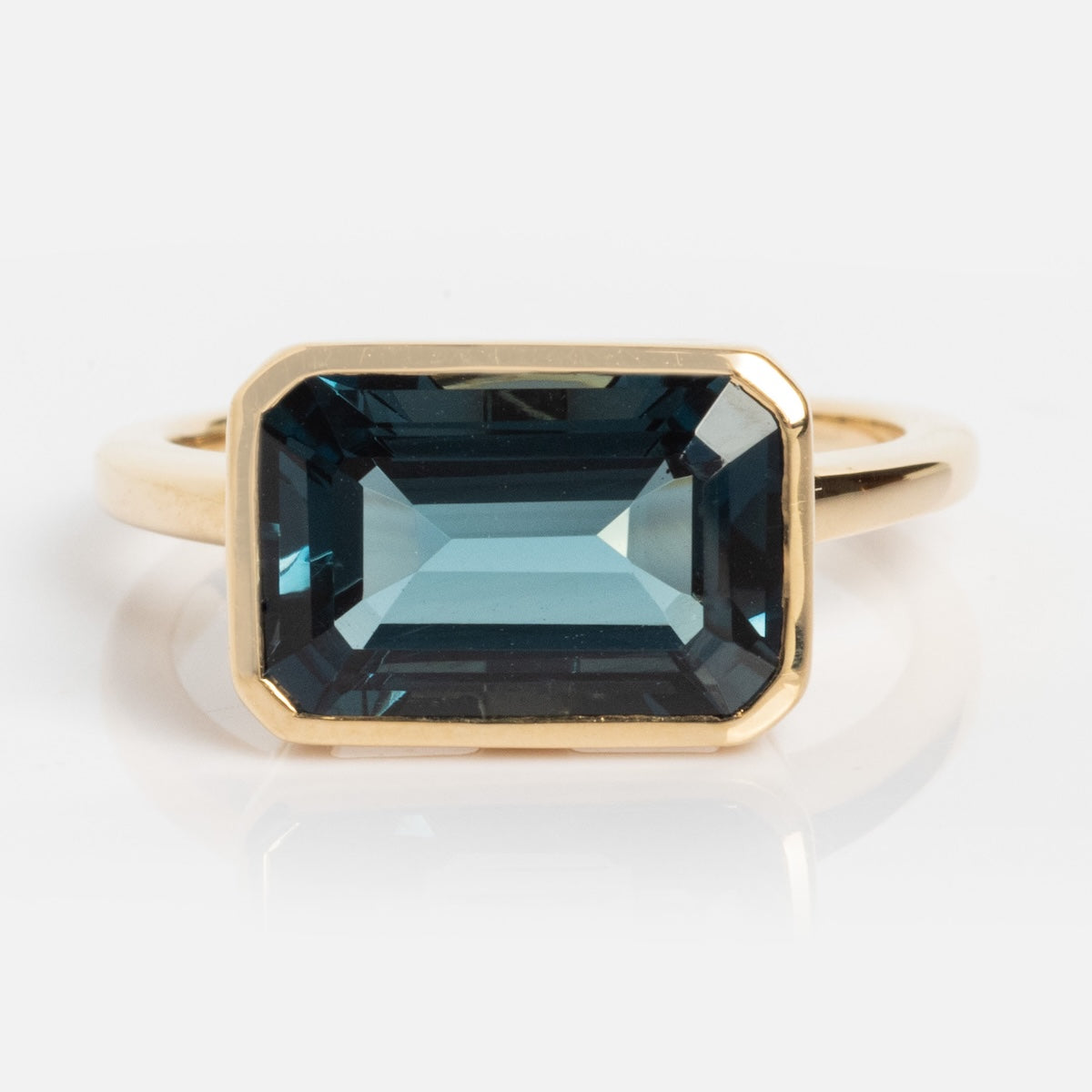 The 14k Jojo Ring is crafted from solid yellow gold and showcases a large, rectangular deep blue gemstone in a bezel setting, displayed on a white background.