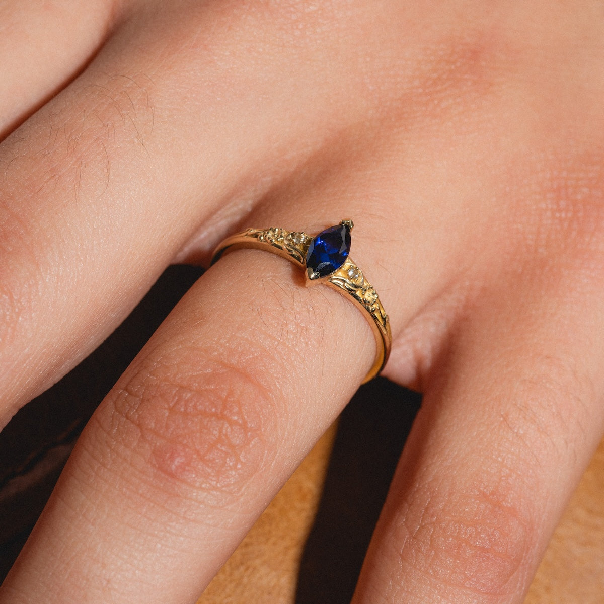 A close-up of a hand wearing the Solid Gold 2025 September Capsule Classic Blue Sapphire Statement Ring, featuring a marquise-cut lab-created blue sapphire and decorative band details, set against a neutral background.