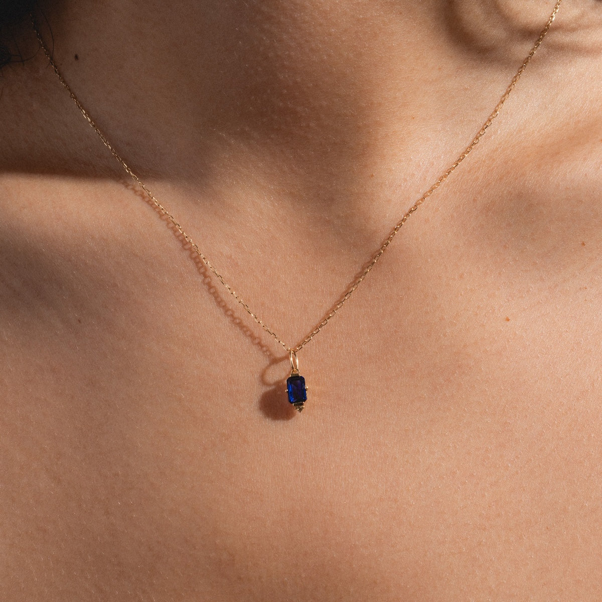 A close-up of a persons bare chest and neck wearing the Solid Gold 2025 September Capsule Classic Blue Sapphire Pendant Necklace.