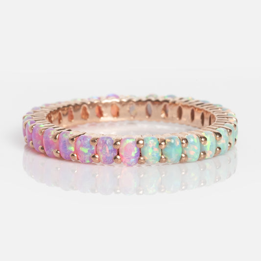 The Opal Ombre Dual Band is a gold ring featuring oval opal gemstones in a continuous band, showcasing pink, blue, and green hues against a white background.