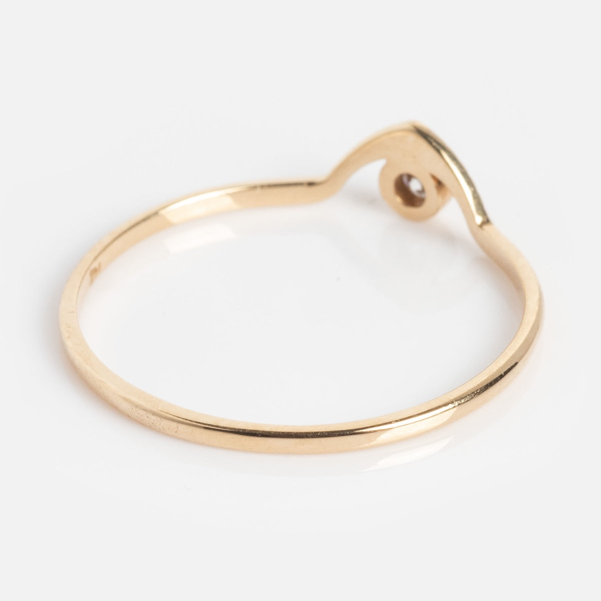 The Corrie Ring is a thin gold band with a simple, modern design and a small looped detail on one side, displayed on a plain white background.