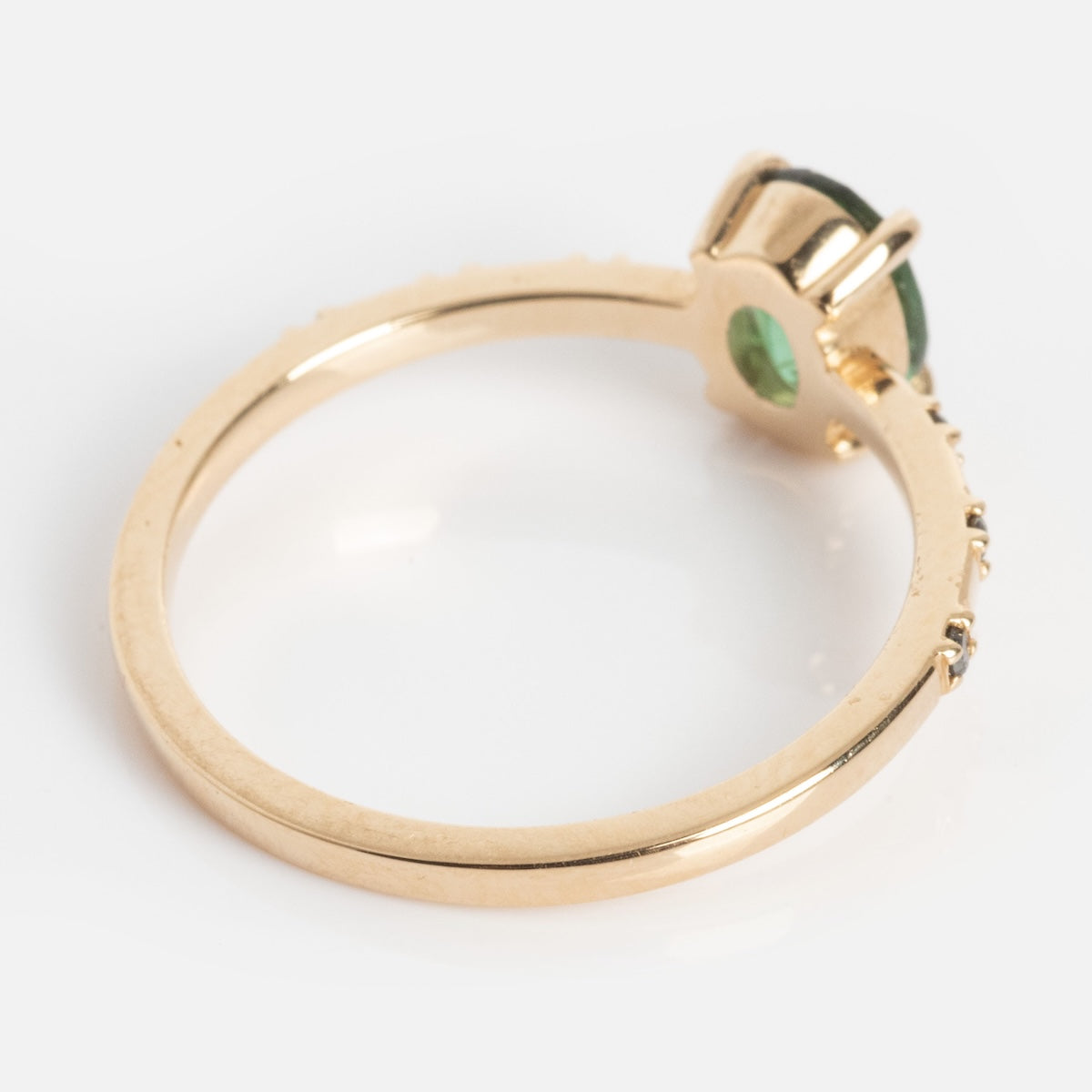 The Iona Ring Black Diamond Ring is crafted from 14k yellow gold, featuring a round black diamond in a prong setting and small accent stones along part of the band, shown from the side against a white background.