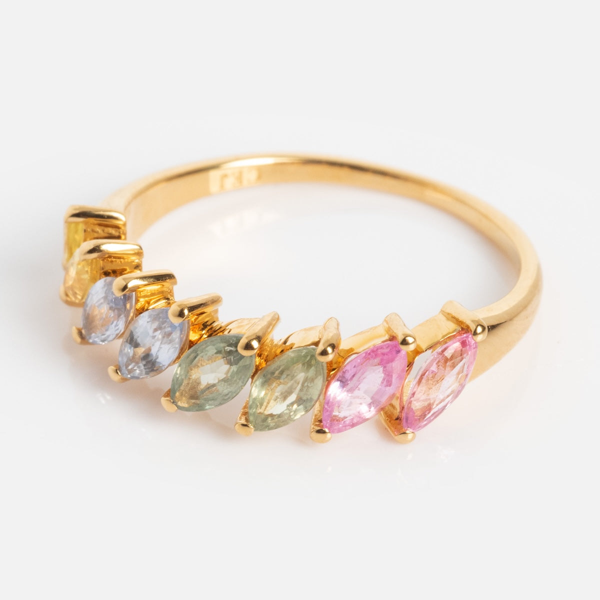 The Della Rainbow Sapphire Ring is a gold band adorned with seven marquise-cut sapphires in yellow, blue, green, and pink, arranged in a row against a white background.