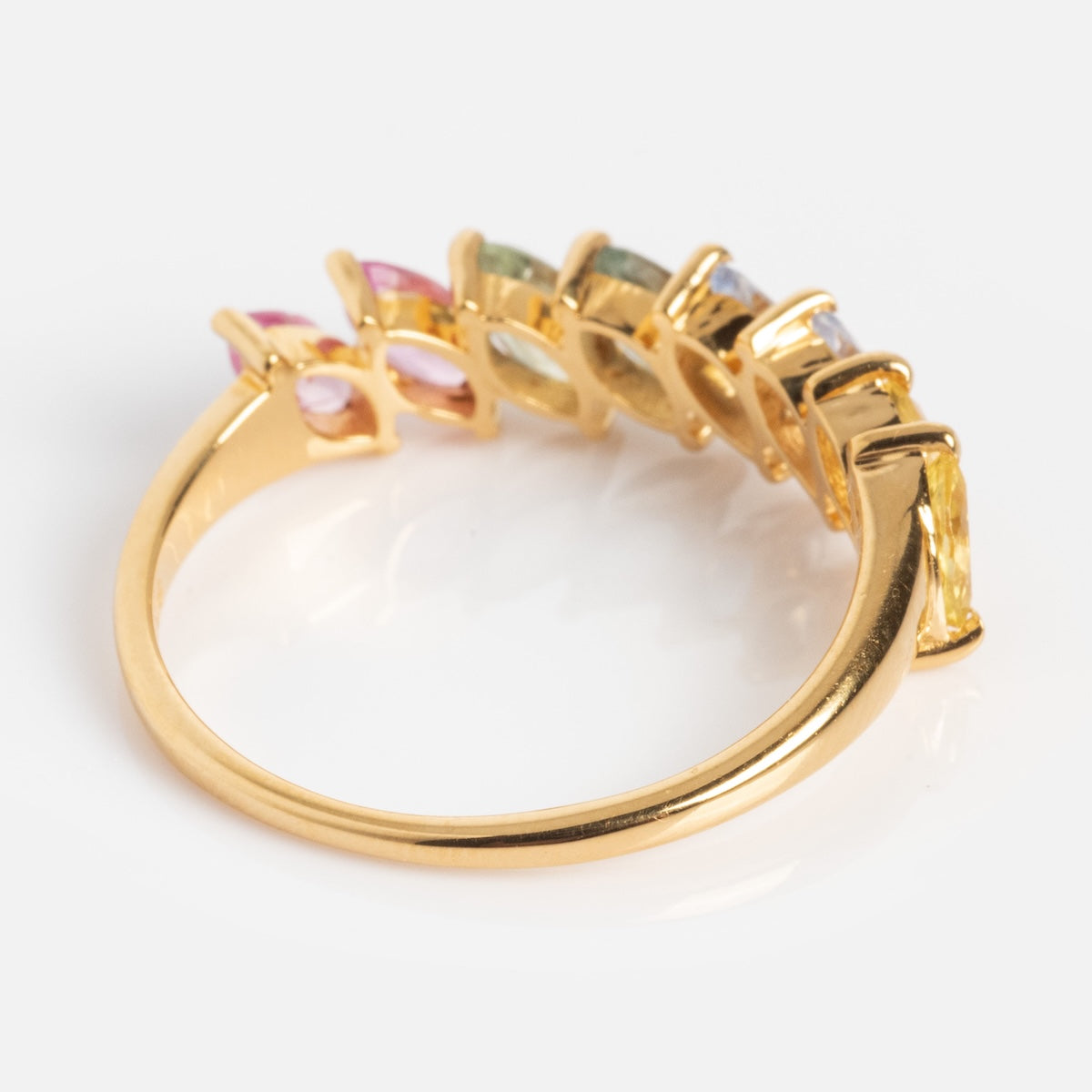 The Della Rainbow Sapphire Ring is a gold band with pink, green, blue, and yellow sapphires set in a curved row along the top half, shown on a white background.