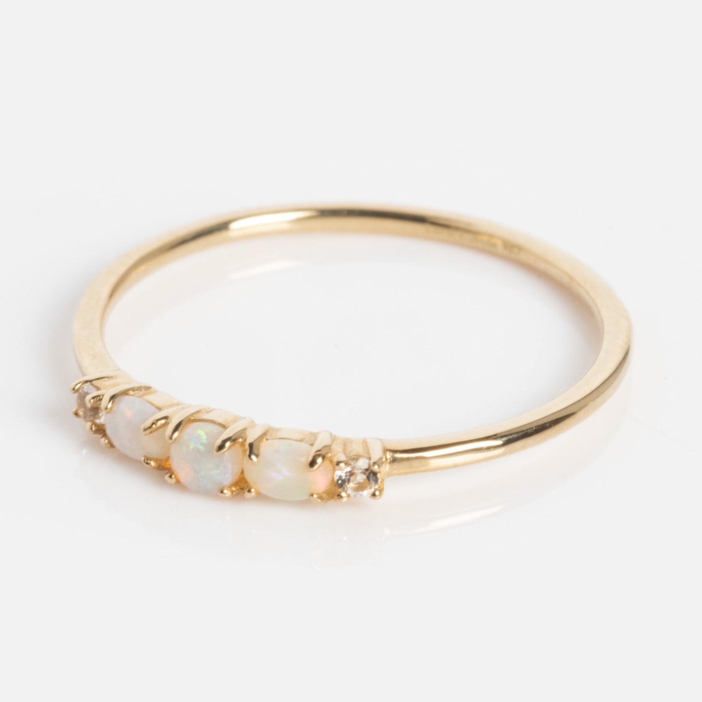 The Solid Gold 2025 October Capsule Classic Opal Trio Statement Ring showcases three oval opals and two clear gemstones set in a row on a slim gold band, displayed on a plain white background.