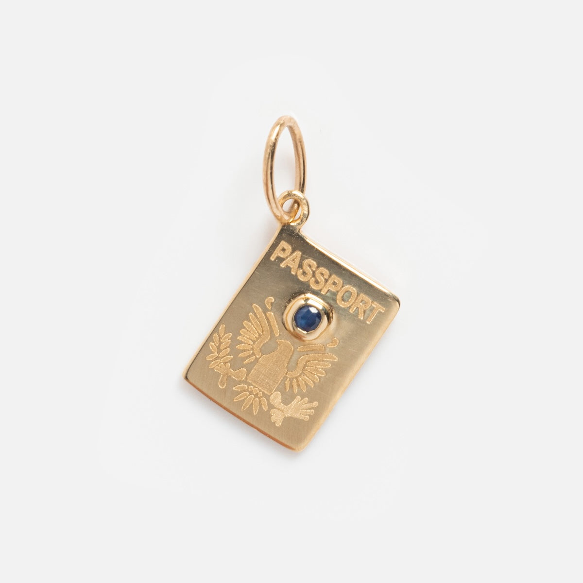 The Solid Gold Celebration Charm is a 9k yellow gold pendant shaped like a passport, engraved with an eagle and set with a blue gemstone at its center, featuring a small loop for attaching to a chain—a unique engraved gold charm.