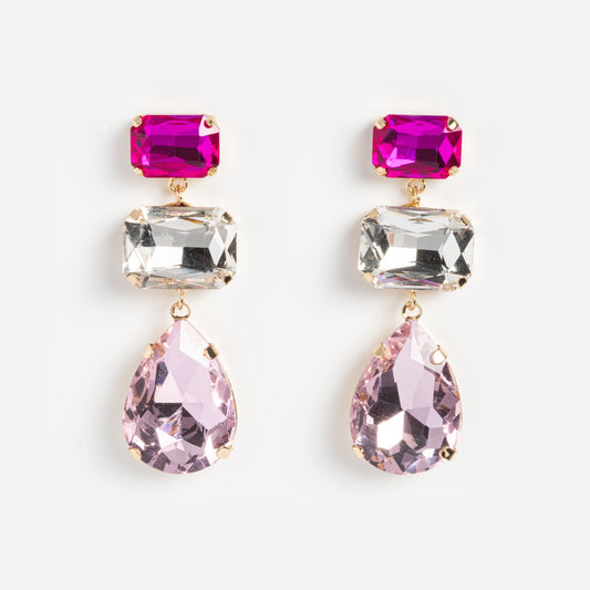The Alexi Earrings feature three gem drops—a rectangular fuchsia stone, a clear rectangular gem, and a teardrop-shaped light pink stone—set in gold. These sparkling statement earrings are perfect for elevating any look.