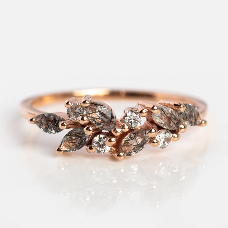 The Gemstone Orchard Ring showcases a cluster of marquise and round-cut London blue topaz and clear diamonds in a rose gold, leaf-inspired design on a sleek band.